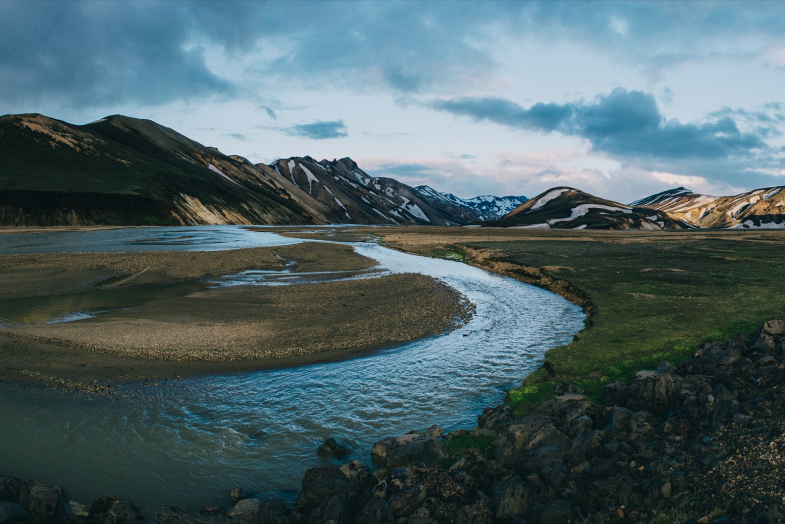 Glacial river curving through Landmannalaugar, Iceland with snow-streaked rhyolite ridges behind