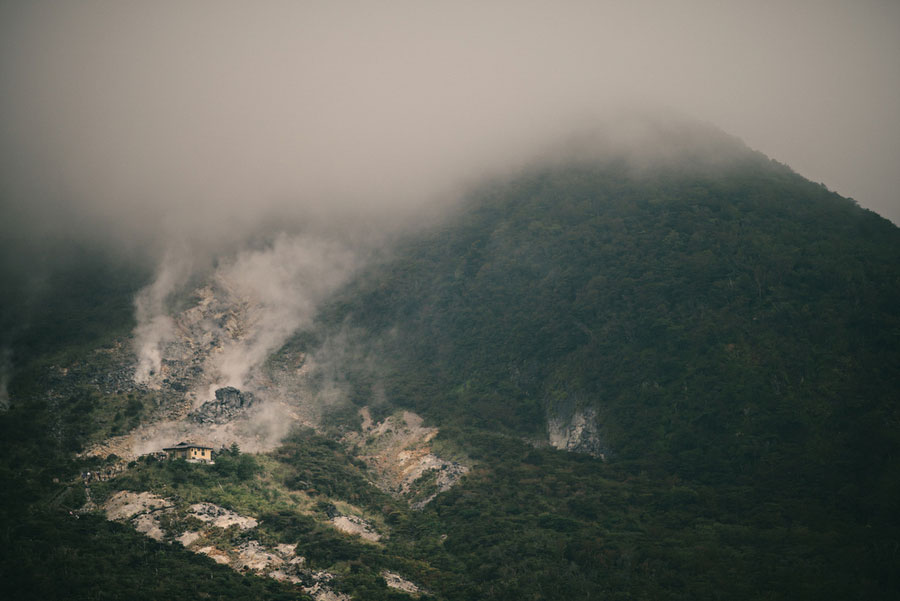 Volcanic steam rising from the forested slope of a mountain shrouded in fog