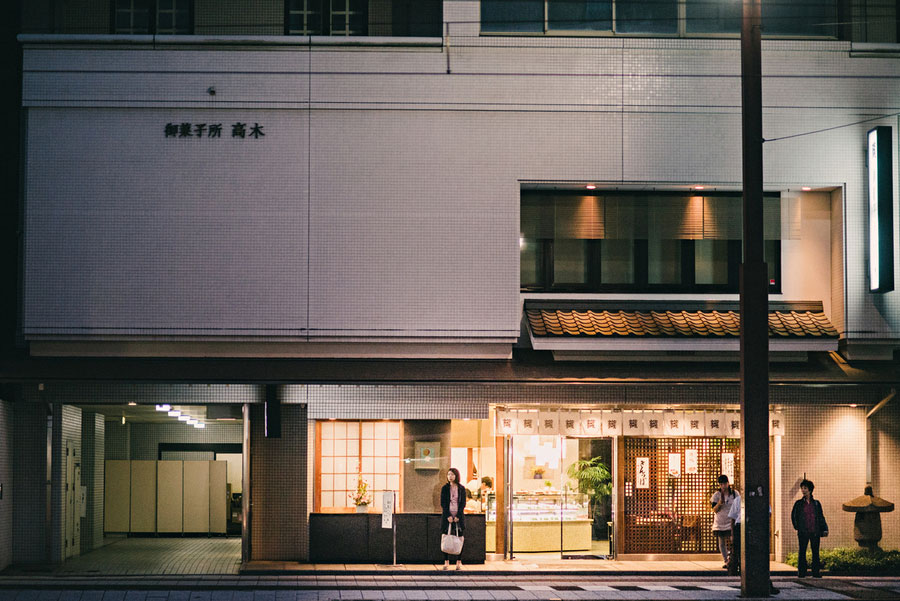 Illuminated traditional Japanese confectionery shop at night with customers at the entrance