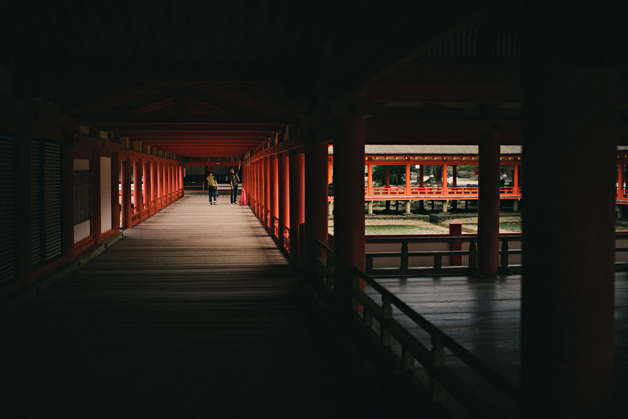 Red-pillared covered corridor of Itsukushima Shrine with visitors walking along the wooden walkway
