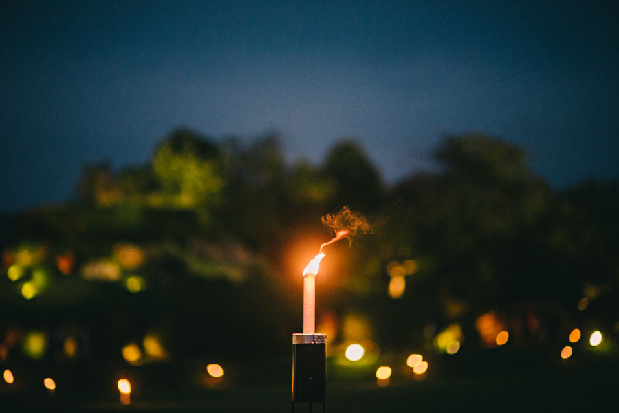 Single flame torch burning against a twilight sky with bokeh garden lights in the background