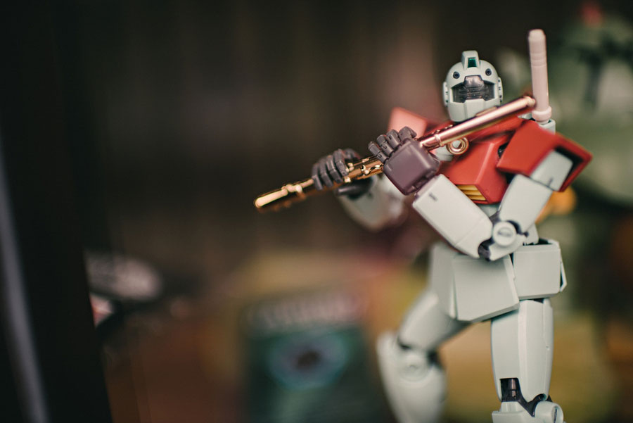 Close-up of a Gundam model figure in a dynamic pose with a rifle in a display case