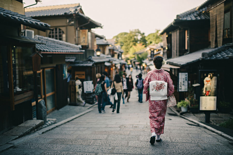 Woman in a pink kimono walking away down a traditional Kyoto shopping street