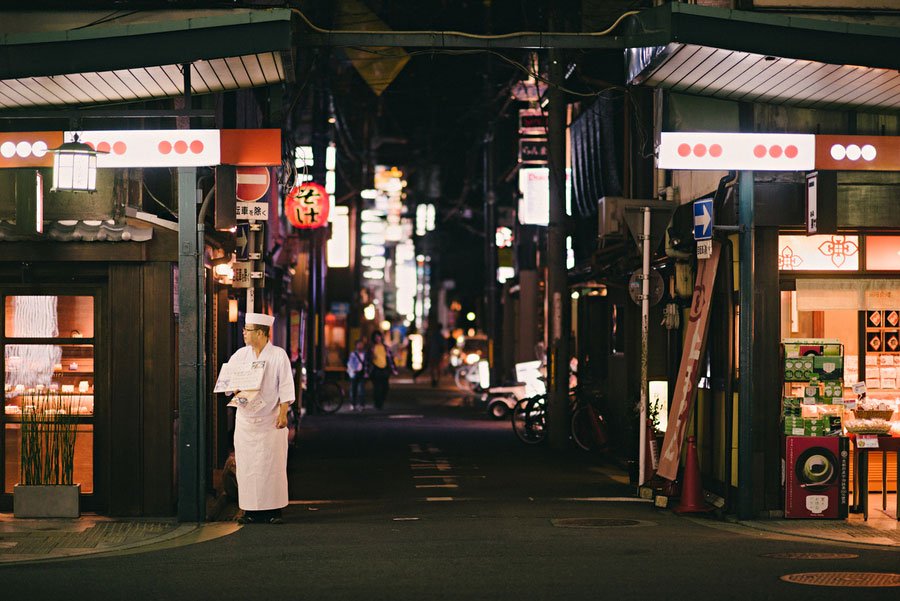 Chef in white standing in a narrow lantern-lit alley at a Kyoto market late at night