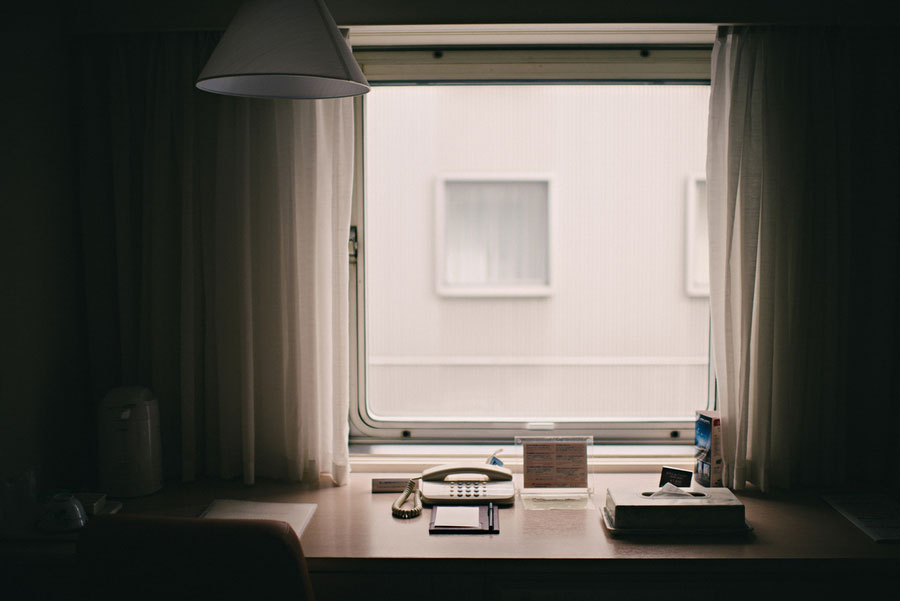 Minimal Japanese hotel room desk with telephone and lamp beside a curtained window