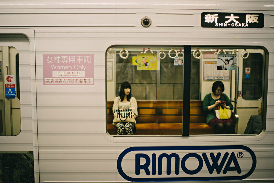 Two passengers seen through the window of a Shin-Osaka subway car with Women Only signage
