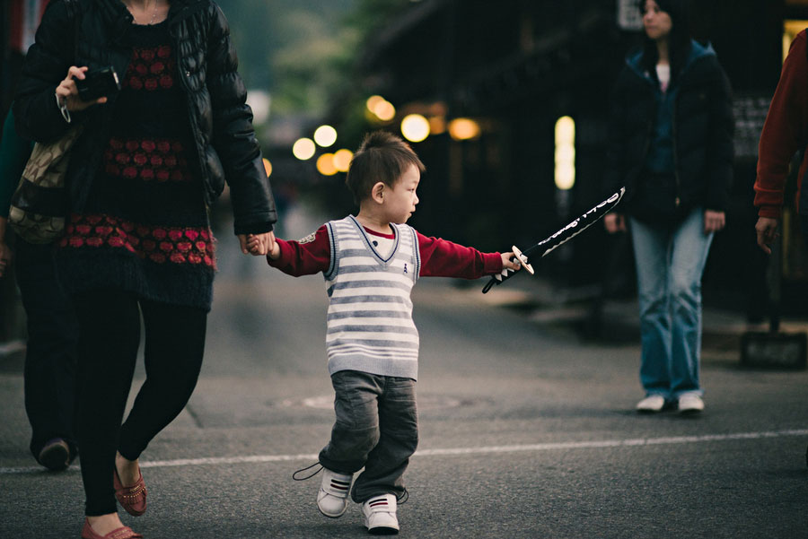 Toddler holding a toy sword walking across a rainy street holding a parent's hand