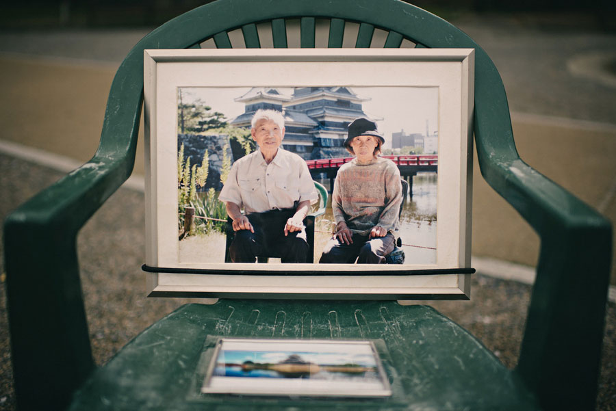 Framed photograph of an elderly couple sitting on a green chair displayed on a street