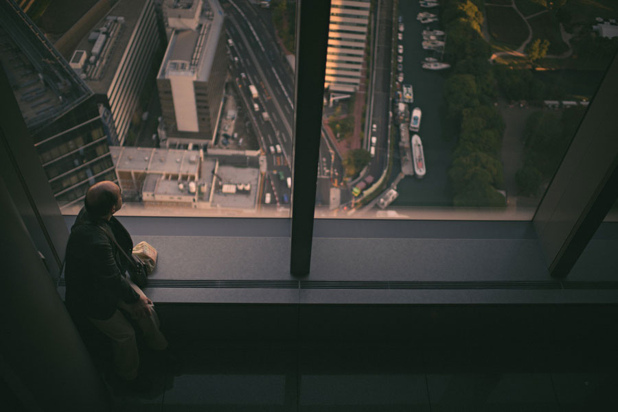 Person looking down through a high-rise glass floor at the streets and rail lines far below