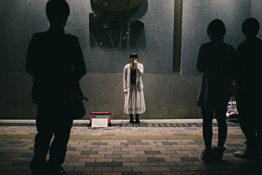 Street singer performing with a microphone at night while silhouetted passersby watch