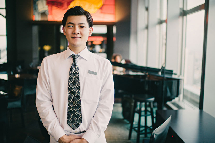 Young Japanese man in a white shirt and patterned tie standing in a restaurant with warm light